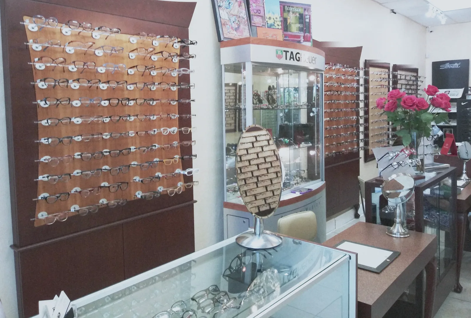 La pared de monturas sobre madera, la vitrina de TAG Heuer y un ramo de rosas en el mostrador