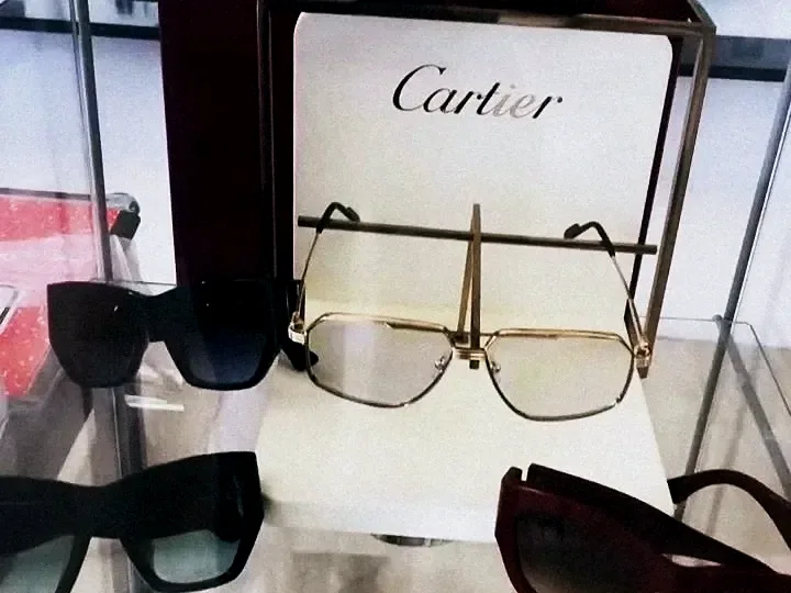 Monturas doradas y gafas de sol Cartier en una repisa de cristal, con el letrero de Cartier