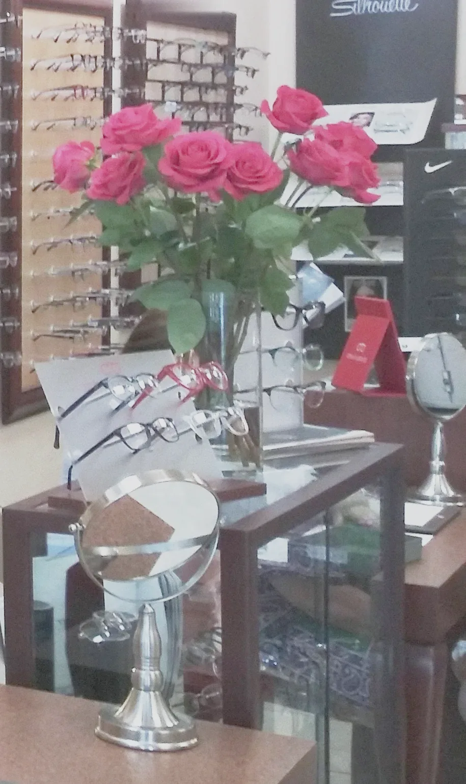 Rosas rojas en un jarrón de cristal sobre el mostrador, con un espejo y monturas alrededor